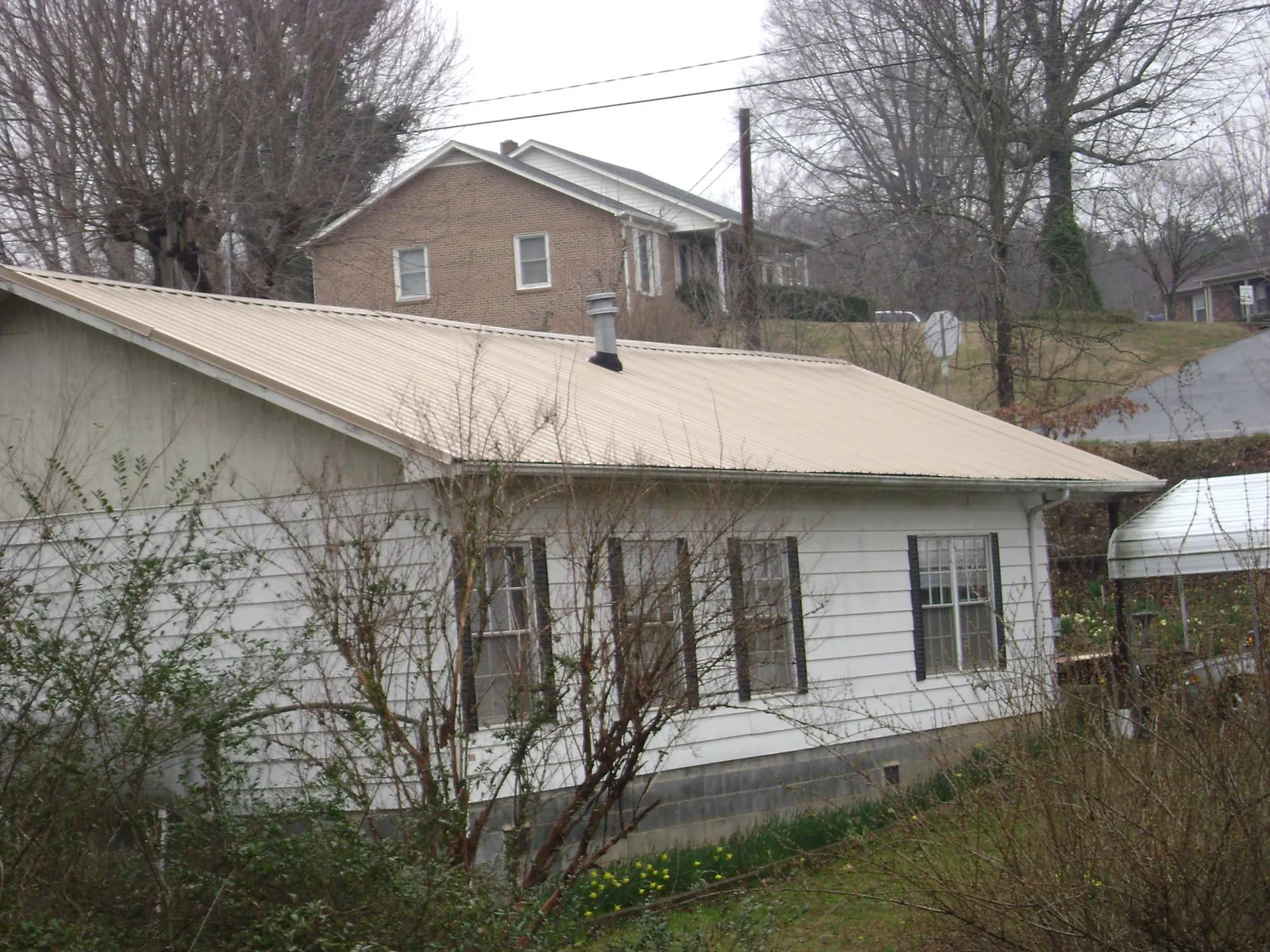 Tan metal roof on a white sided house set into a hillside — Commercial Roofing by Roofing Brothers in Cornish